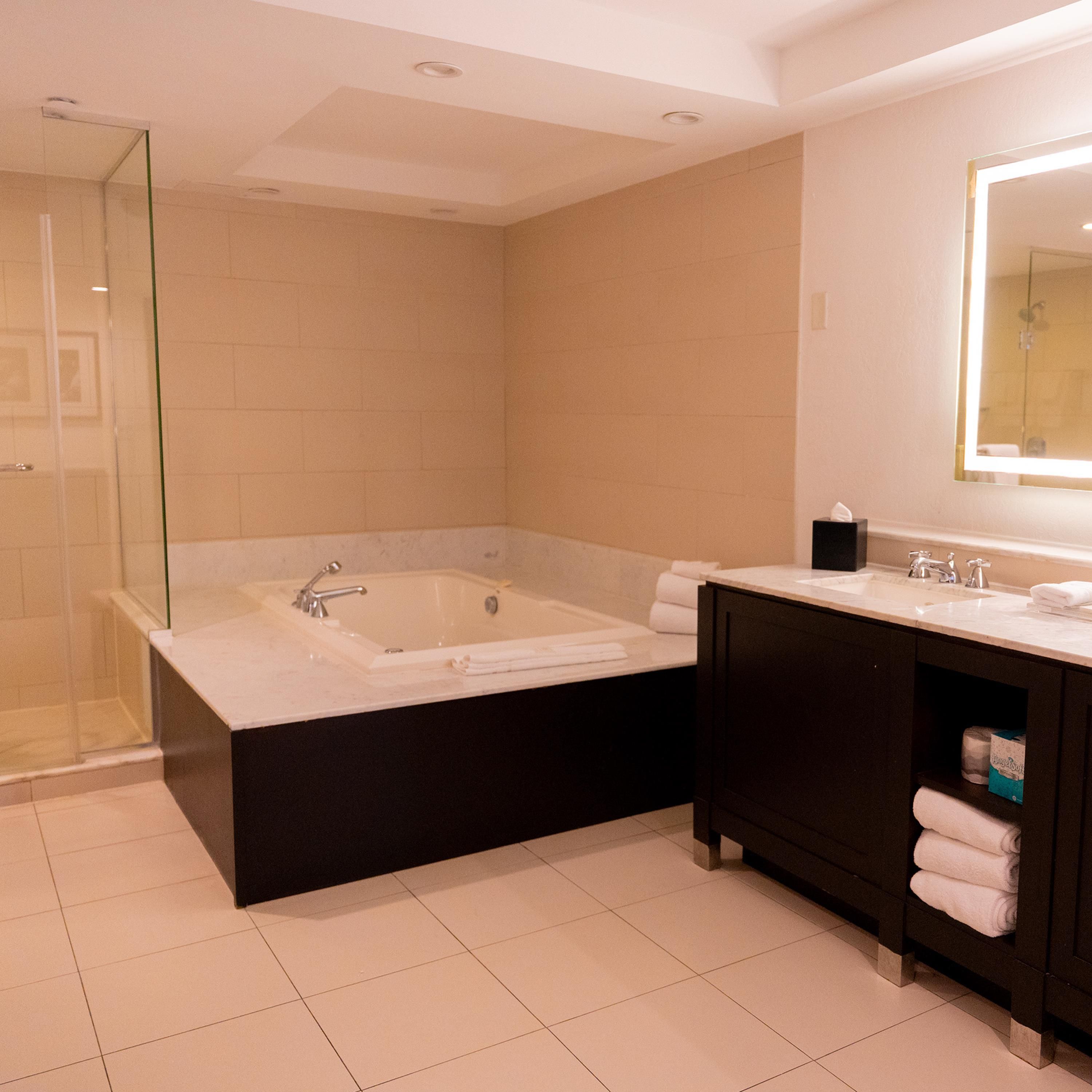 Une salle de bain moderne avec une douche à parois de verre, une baignoire sur pieds et un meuble-lavabo foncé doté d’un miroir.