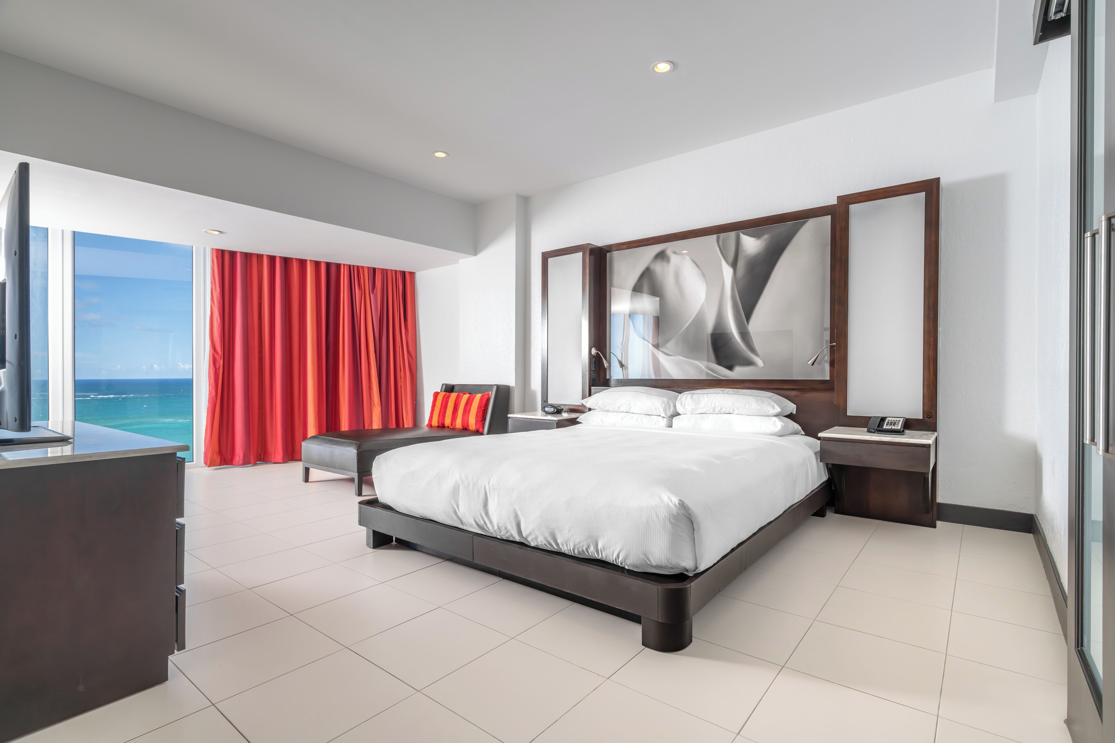 A modern hotel room with a large bed, a desk, and a view of the ocean.
