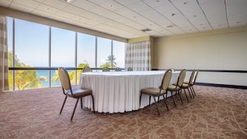 Un salón de conferencias con una mesa redonda, seis sillas, vista al océano y una alfombra estampada.