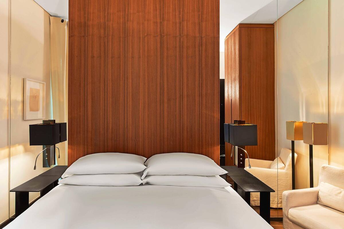 A hotel room with a large bed, two bedside tables, a wooden headboard, a sofa, and two floor lamps.