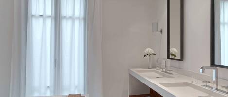 A modern bathroom with two sinks, a large mirror, and a window with sheer curtains.
