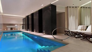 A modern indoor swimming pool with a clear blue water feature, a lounge area with white cushioned chairs, and a large mirror reflecting the pool. - Le Metropolitan Paris Tour Eiffel, a Tribute Portfolio Hotel (Paris)