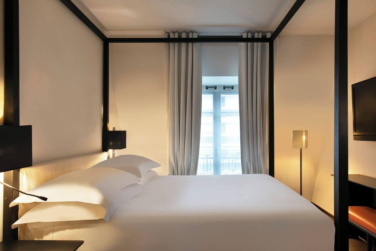 A hotel room with a large bed, a bedside table, a lamp, and a TV on the wall.