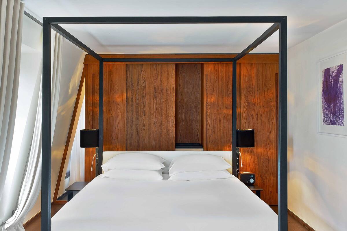 A modern hotel room with a large bed, wooden paneling on the walls, and two bedside tables with lamps.