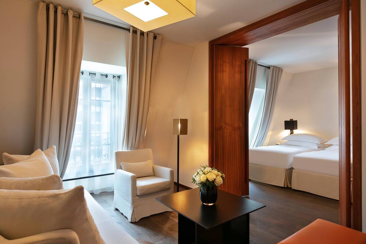 A hotel room with a sofa, a small table with a vase, a bed, and a nightstand.