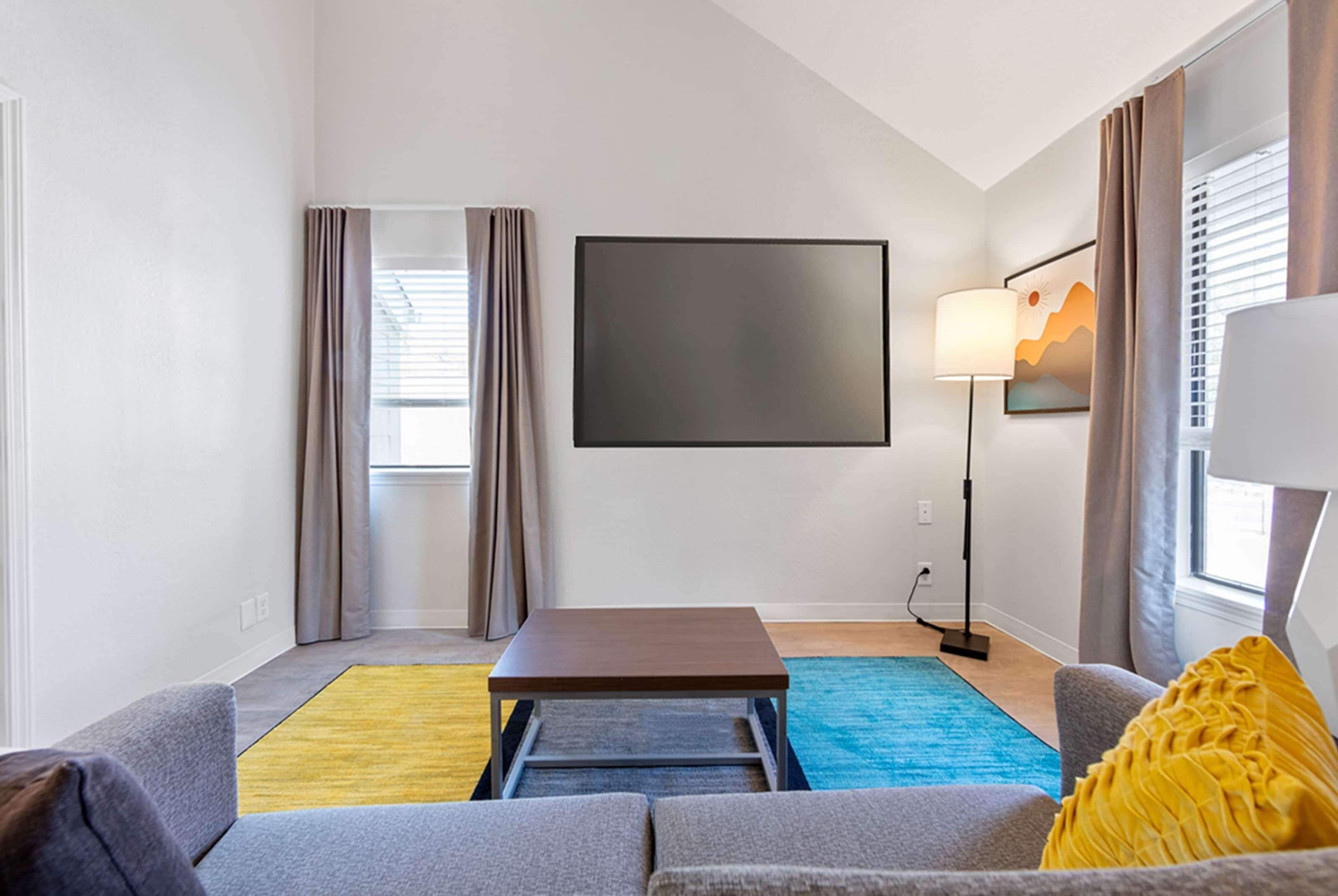 A modern living room with a flat-screen TV, a coffee table, a sofa, and a rug.