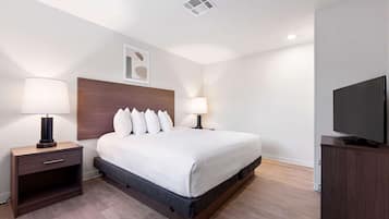 A modern hotel room with a large bed, bedside tables with lamps, a flat-screen TV, and a ceiling vent.