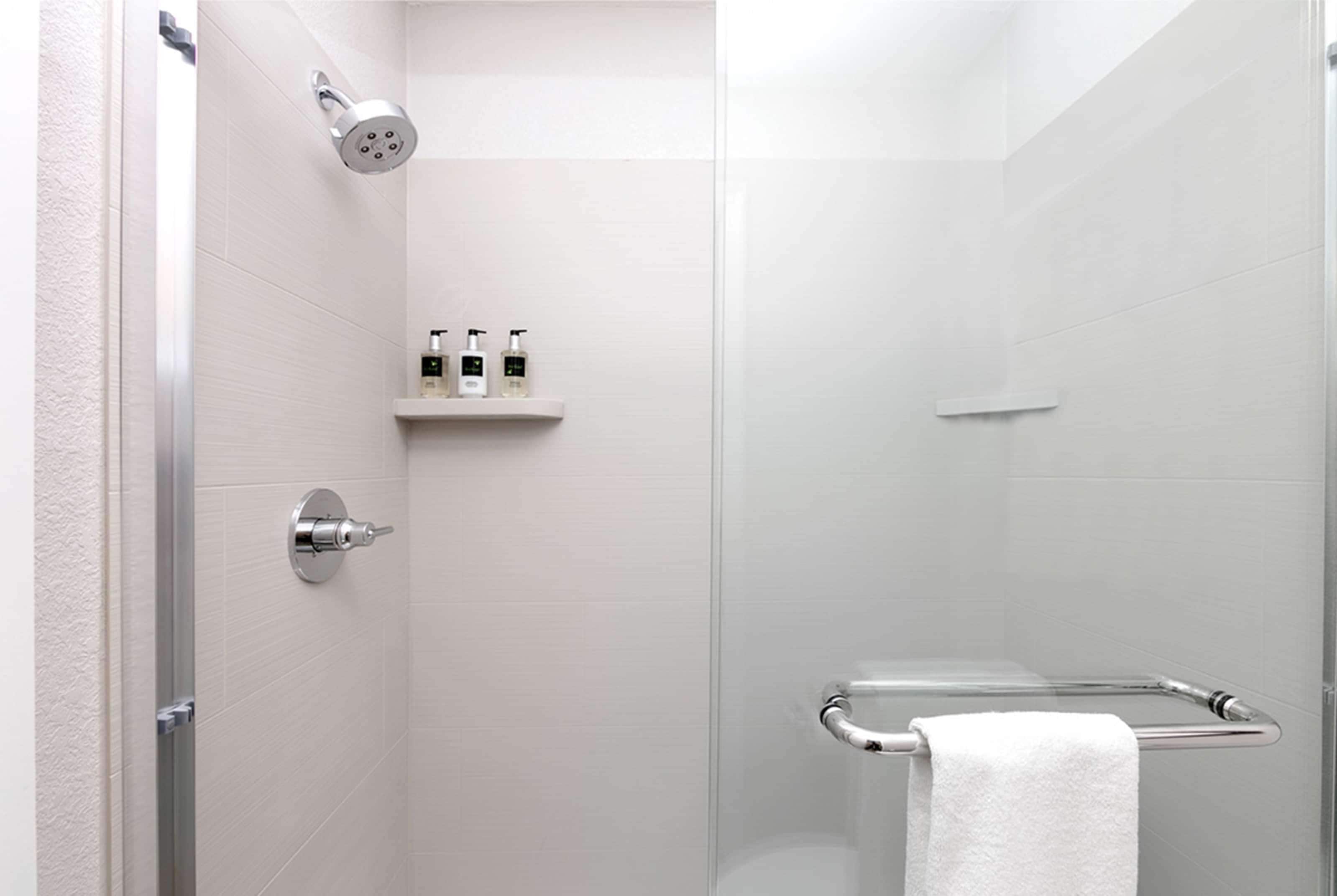 A modern shower with a glass door, a white towel rack, and a shelf with toiletries.