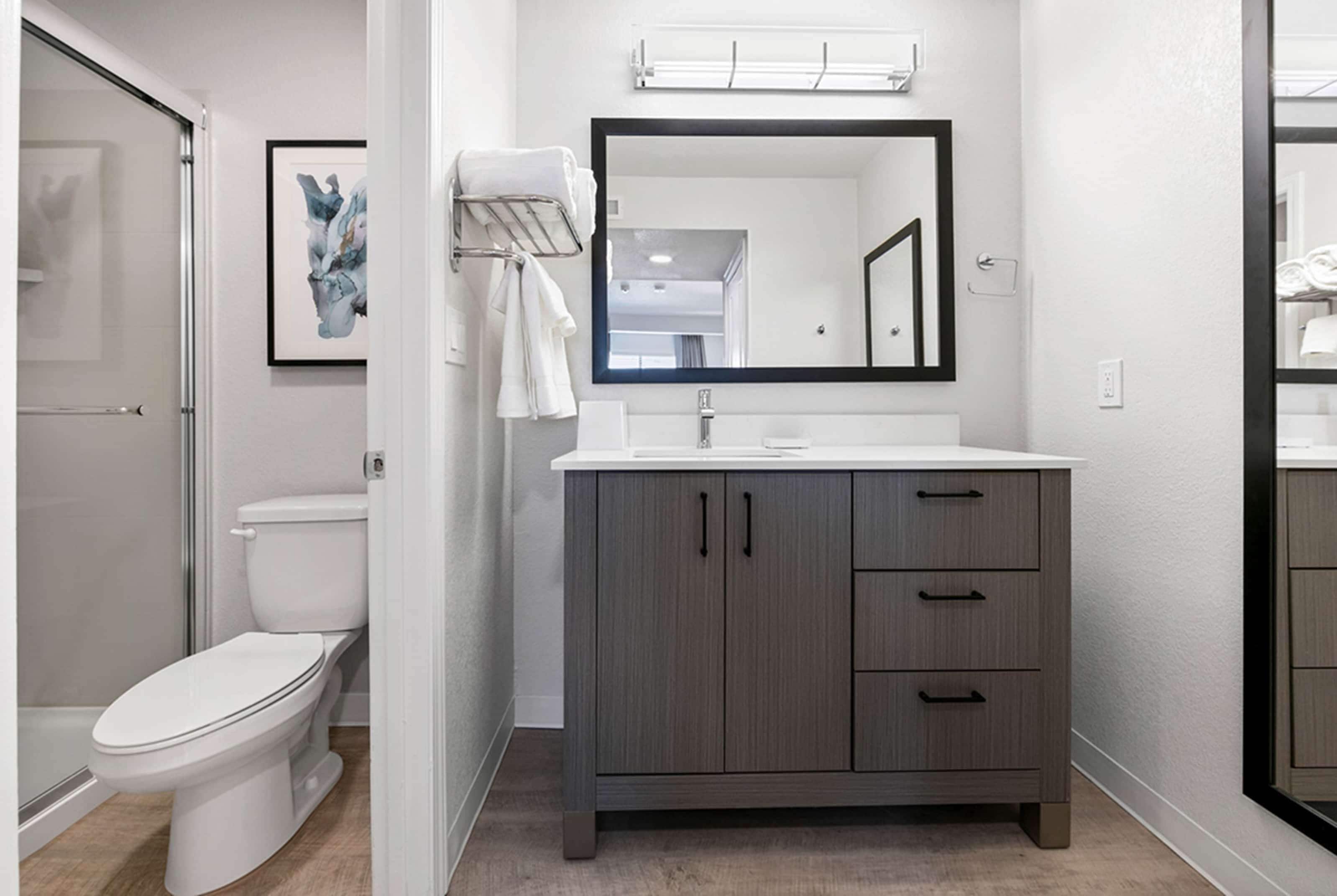 A modern bathroom with a toilet, a vanity with a mirror, and a towel rack.