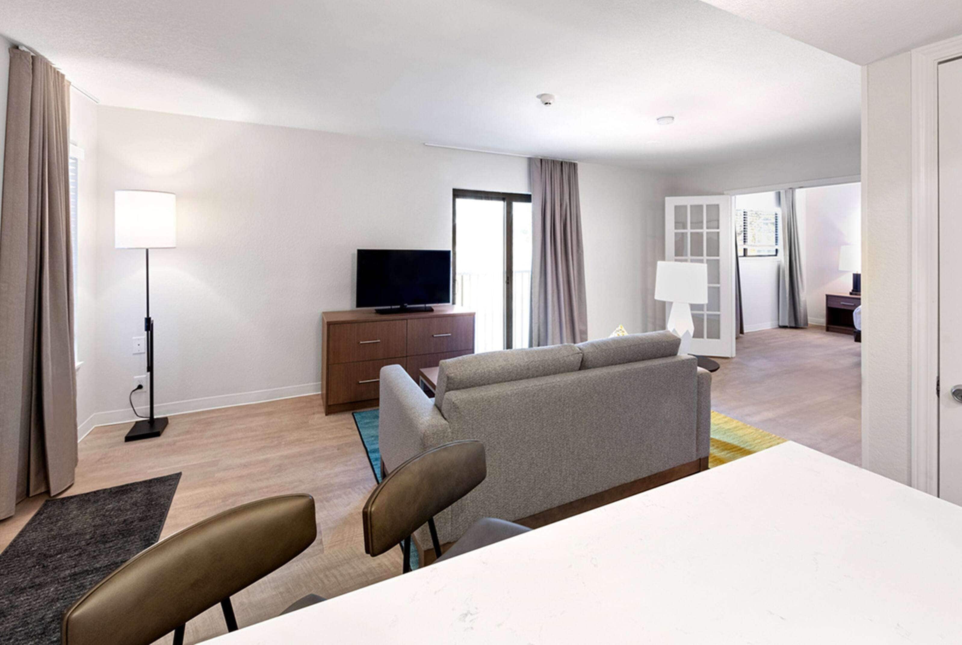 A modern hotel room with a sofa, a flat-screen TV, a desk, and a dining area.