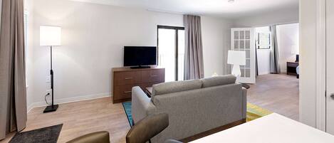 A modern hotel room with a sofa, a flat-screen TV, a desk, and a dining area.