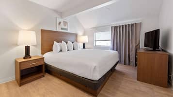Quarto de hotel com uma cama grande, duas mesas de cabeceira com luminárias, uma televisão, uma janela com cortinas e uma luz no teto.