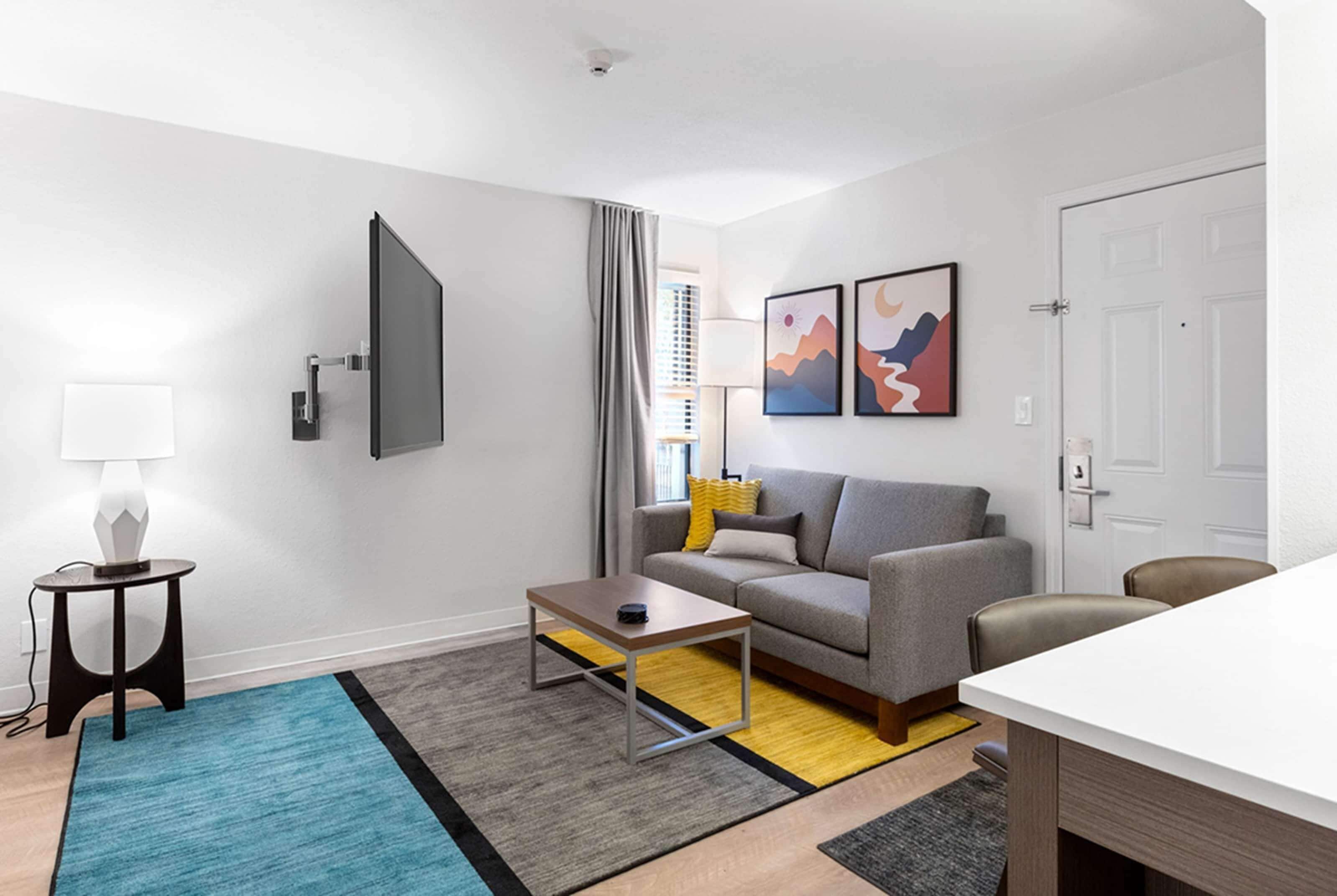 A modern living room with a grey sofa, a coffee table, a TV mounted on the wall, and a door to the right.
