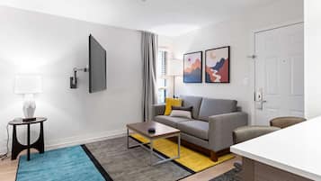 A modern living room with a grey sofa, a coffee table, a TV mounted on the wall, and a door to the right.