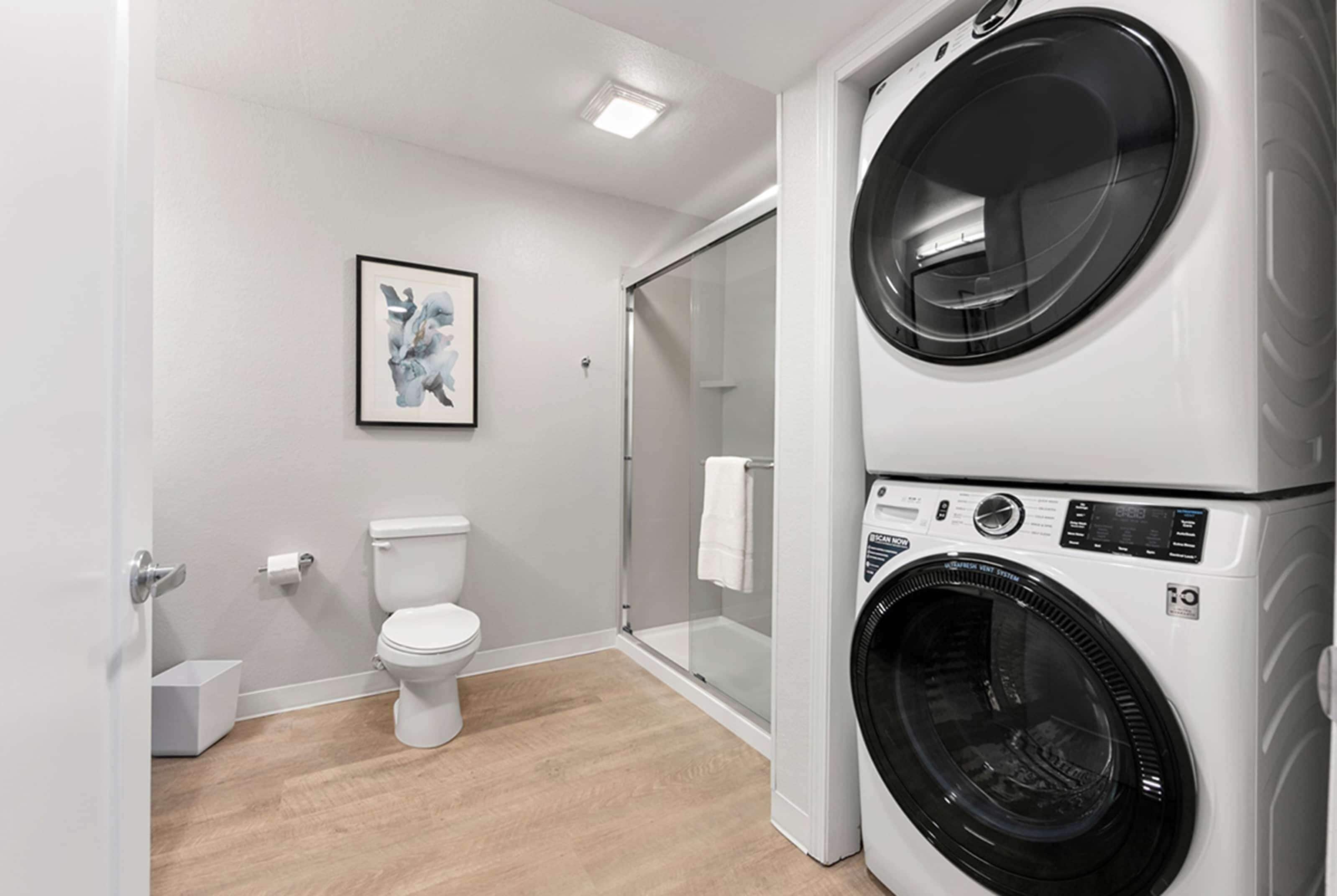 A modern bathroom with a toilet, a shower, and a stacked washer and dryer.