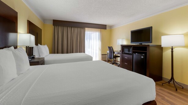A hotel room with two beds, a desk, a television, and a lamp.