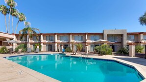 A hotel with a swimming pool, palm trees, and a clear blue sky.