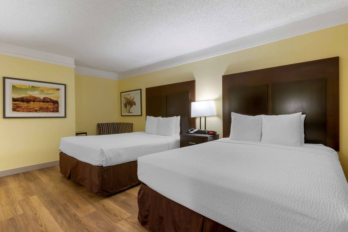A hotel room with two beds, wooden flooring, and a nightstand with a lamp.