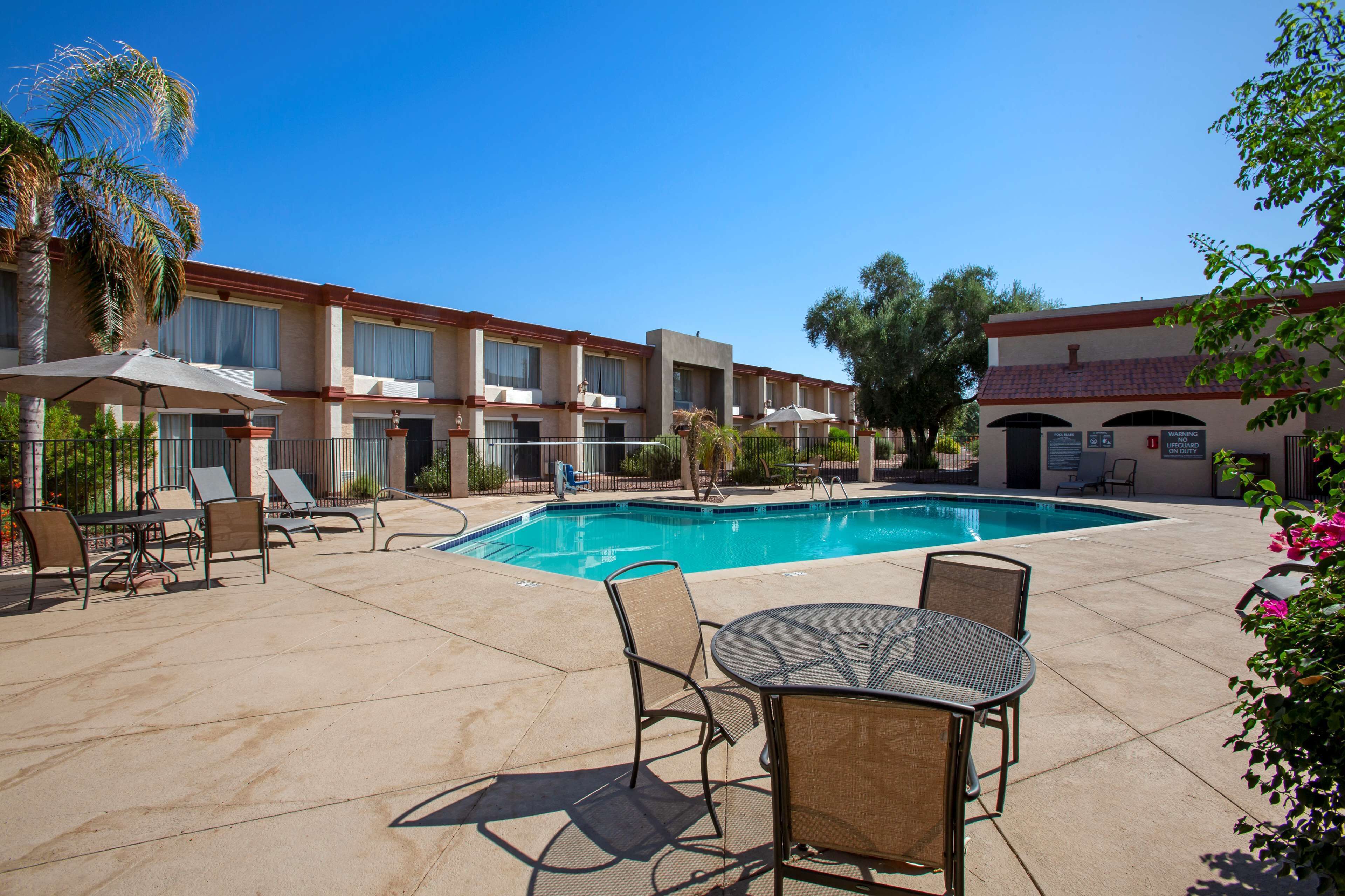 A hotel pool area with lounge chairs, a table, and a sign indicating a lifeguard on duty.