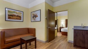 Una habitación de hotel con un sofá de cuero marrón, una pequeña mesa de madera, un armario de madera y dos cuadros en la pared.