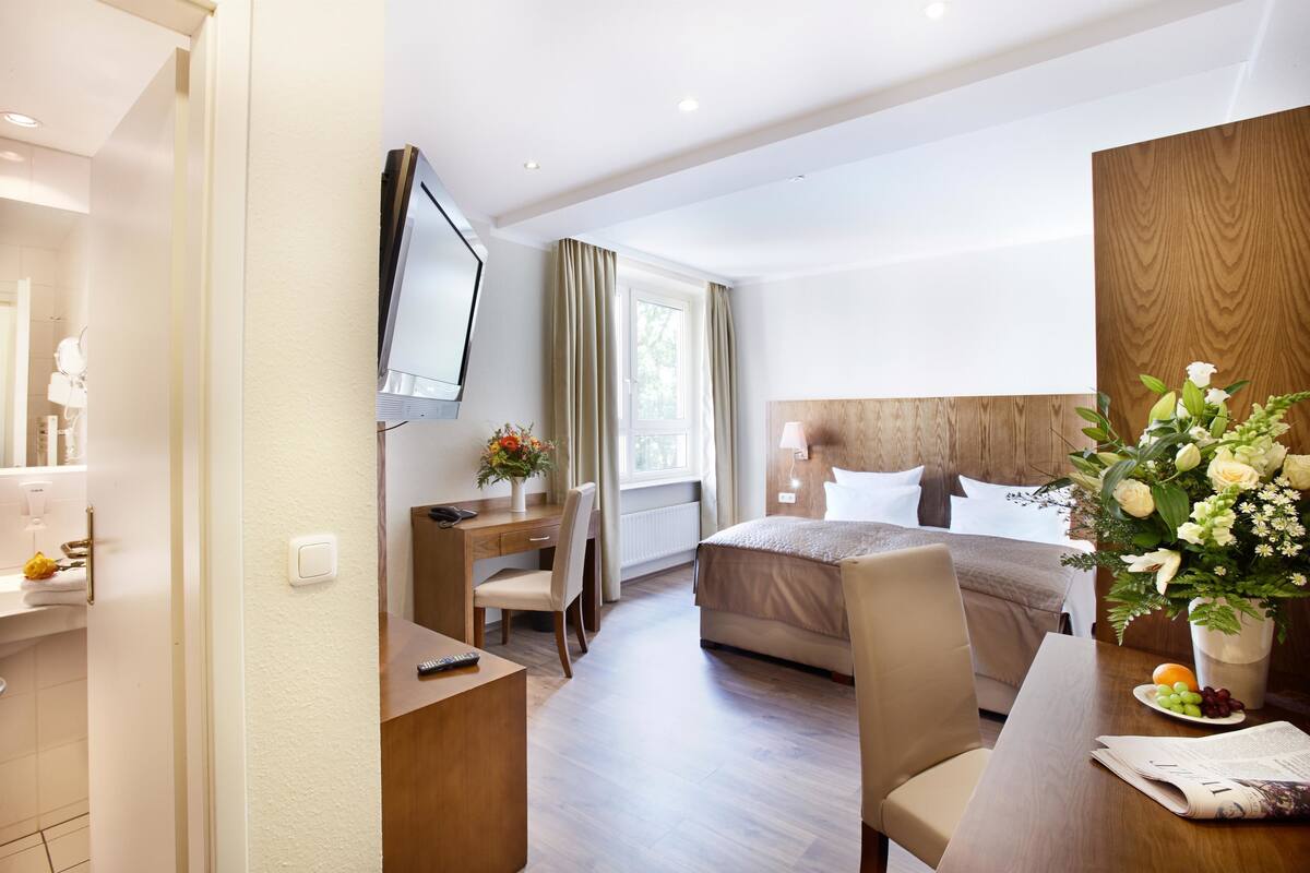 Une chambre d’hôtel équipée d’un lit, d’un bureau, d’une chaise, d’une télévision et d’une fenêtre avec des rideaux.
