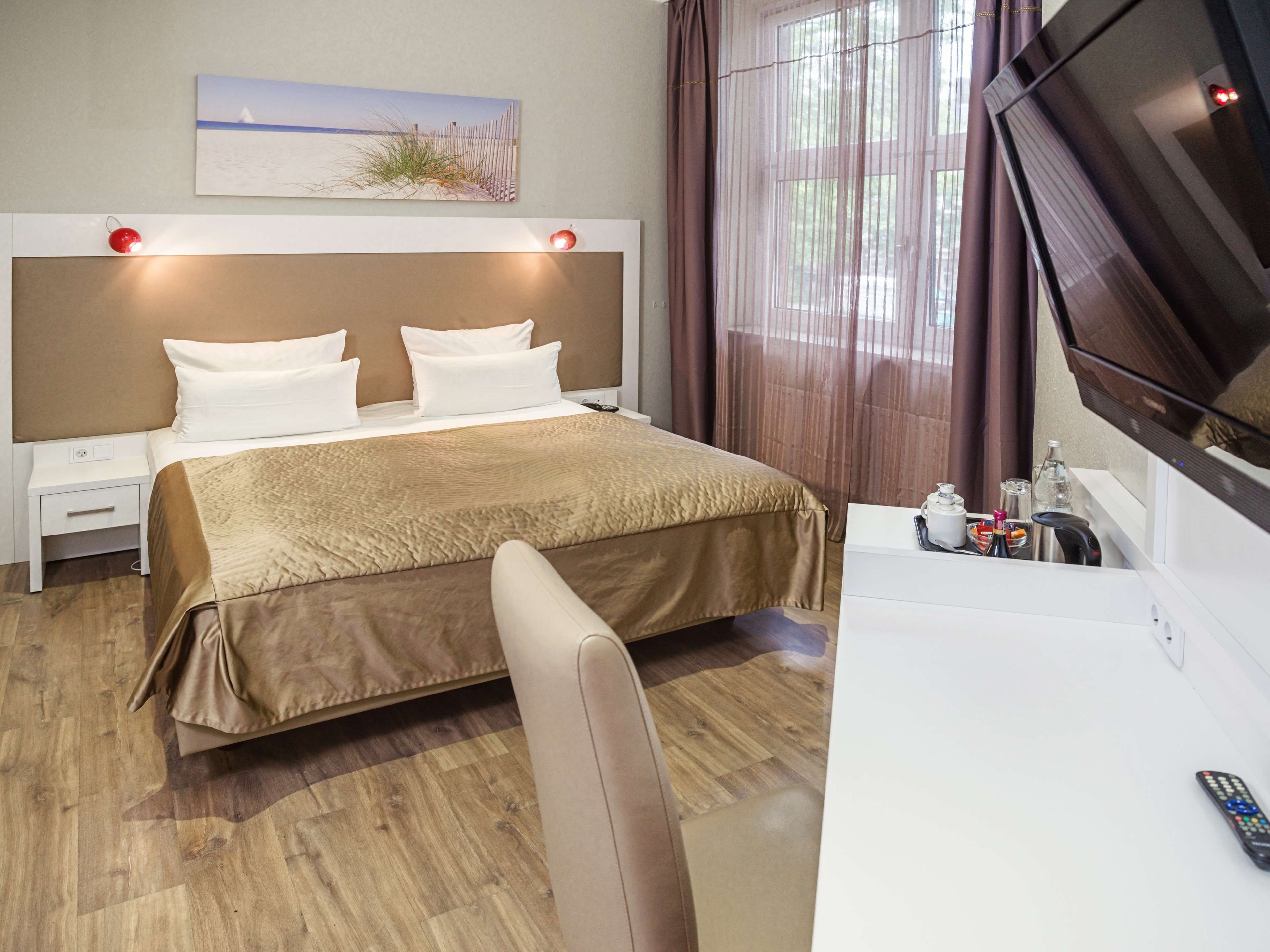 A hotel room with a bed, bedside tables, a desk, a chair, a TV, and a window with curtains.