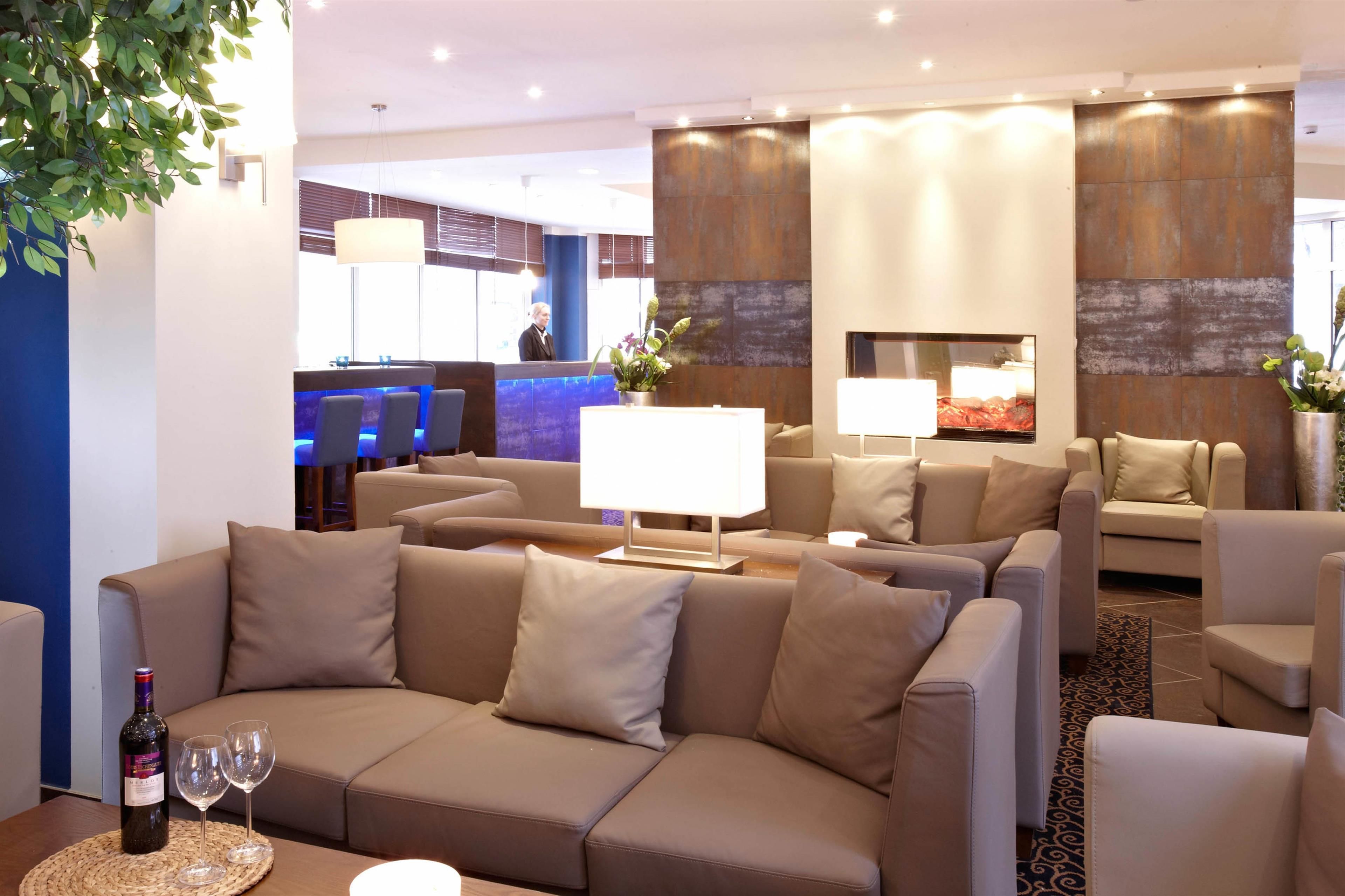 A modern hotel lobby with sofas, a reception desk, and a bar area. - Hotel Domicil Hamburg by Golden Tulip (Hamburg)