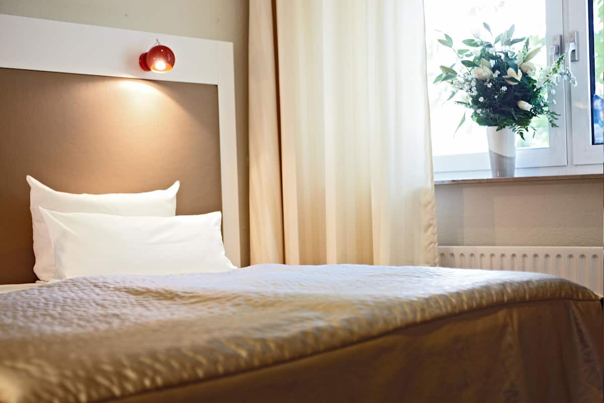 Un lit bien fait, avec des oreillers blancs et une couvre-lit beige, dans une chambre d’hôtel.