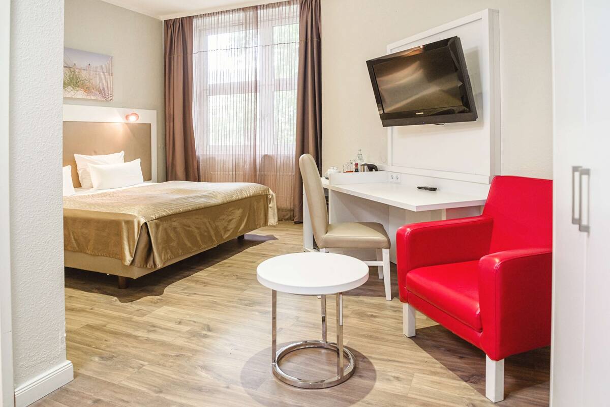 Une chambre d’hôtel équipée d’un lit, d’un bureau, d’une chaise, d’une télévision et d’une fenêtre avec des rideaux.