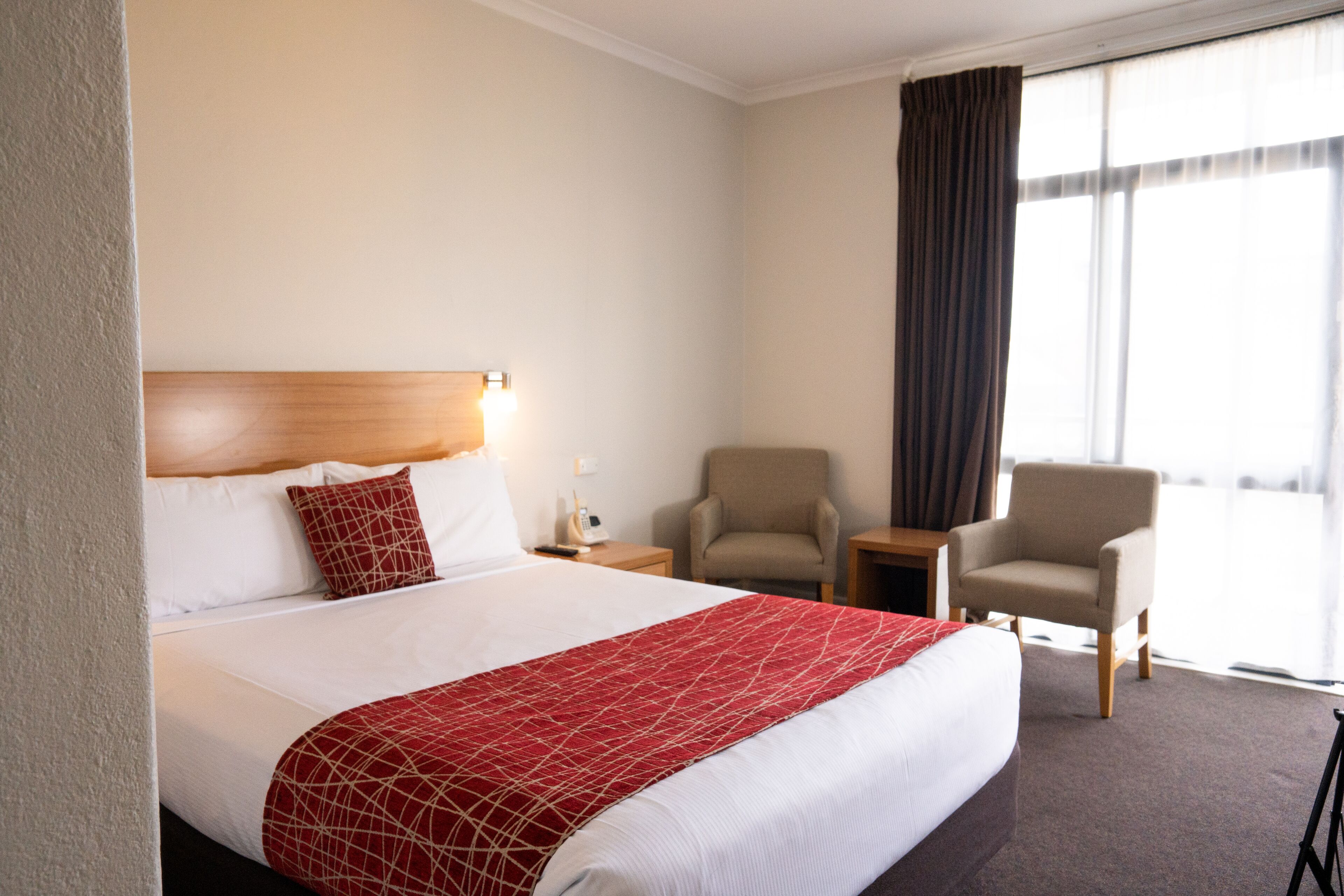 A hotel room with a large bed, two armchairs, a nightstand, and a window with curtains.