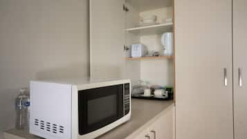 A kitchen with a microwave on the counter, a water bottle, and a cabinet with shelves containing dishes and a toaster.