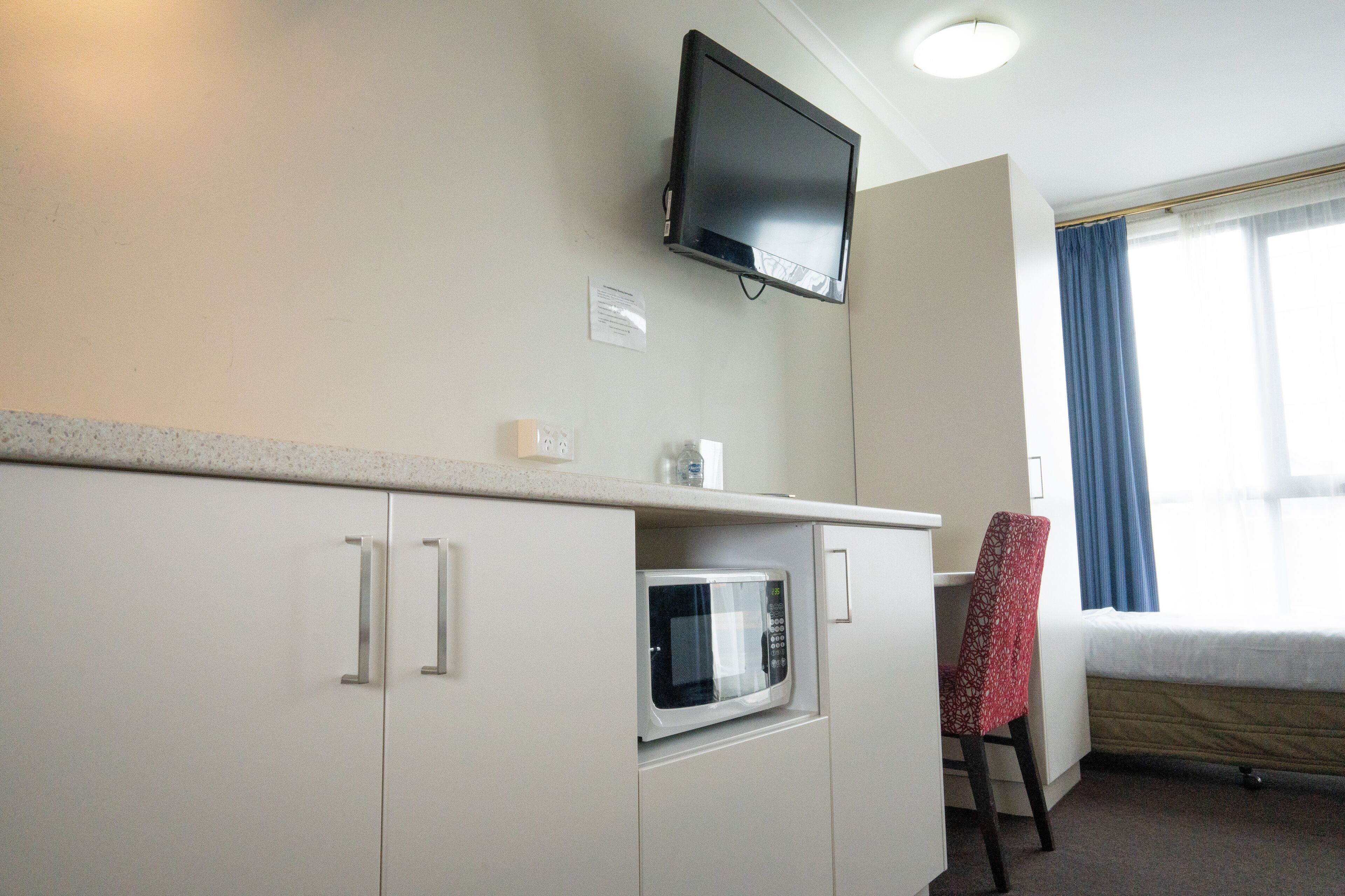 Una kitchenette compacta con microondas, un televisor de pantalla plana montado arriba y una cama con vista al exterior.