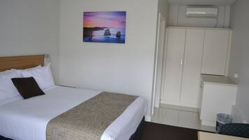 Une chambre d’hôtel avec un lit, un tableau représentant un coucher de soleil, une armoire et un appareil de climatisation.