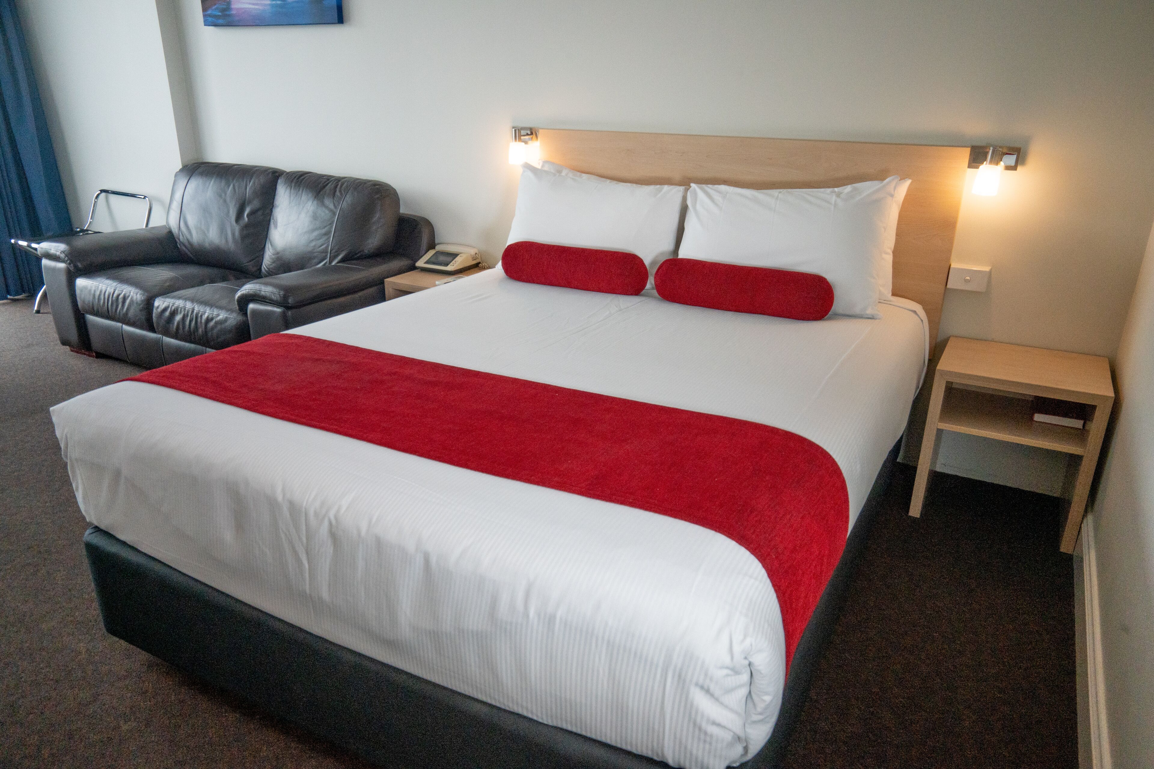 A hotel room with a large bed, a leather sofa, a bedside table, and a nightstand.