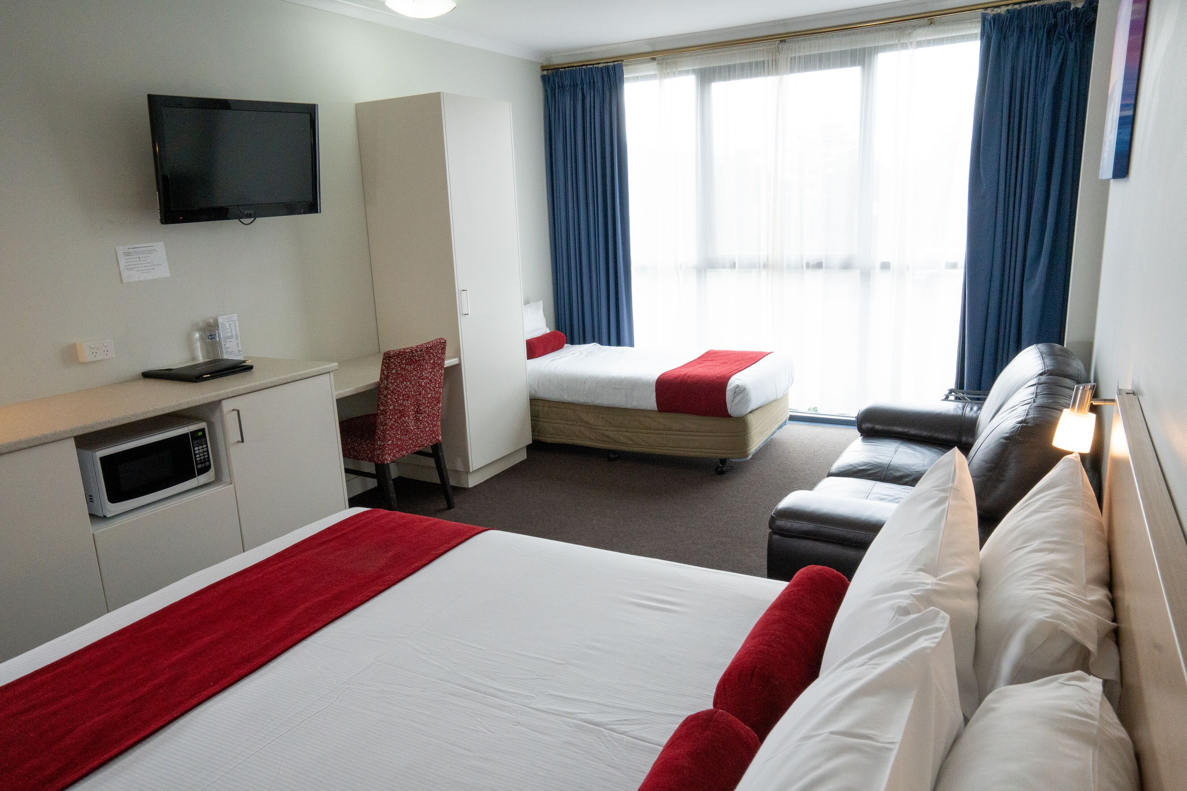 A hotel room with a bed, a desk with a computer, a TV, and a window with curtains.