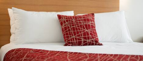Un lit bien fait, avec une literie blanche et rouge, une tête de lit en bois et un luminaire fixé au mur.