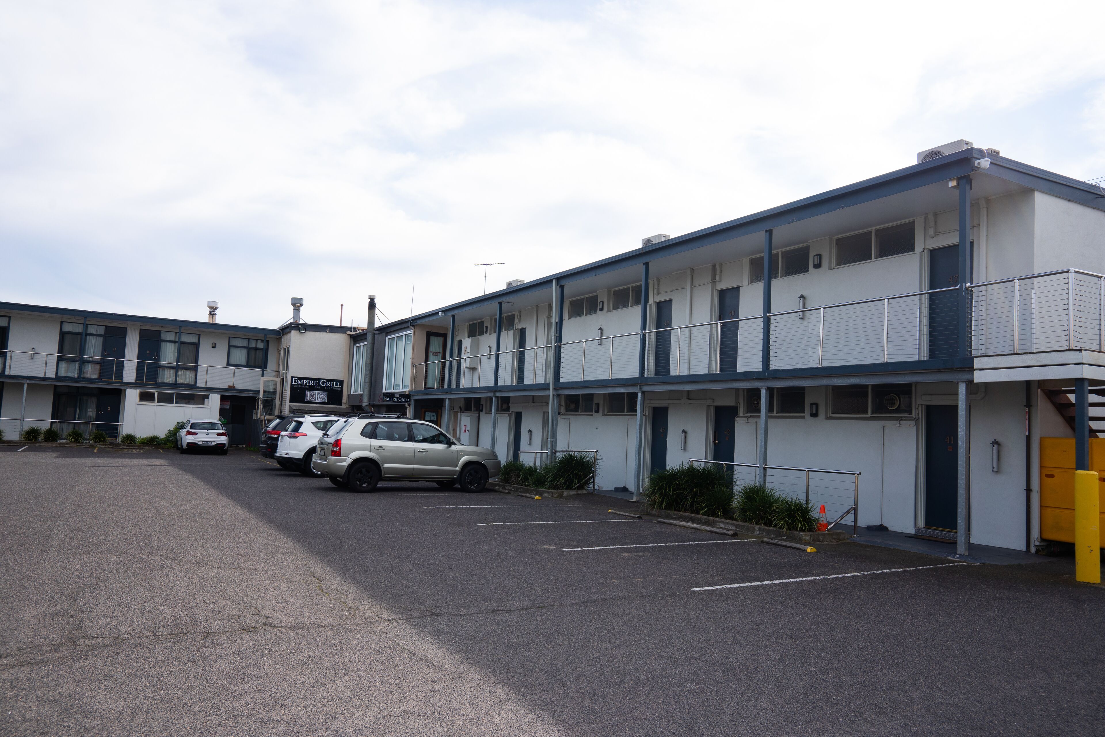 A multi-story motel with a parking lot, several cars parked, and a sign for 'Empire Grill'.