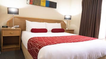 Quarto de hotel com uma cama grande, duas mesas de cabeceira, um criado-mudo, um edredom vermelho e branco, e uma pintura na parede.