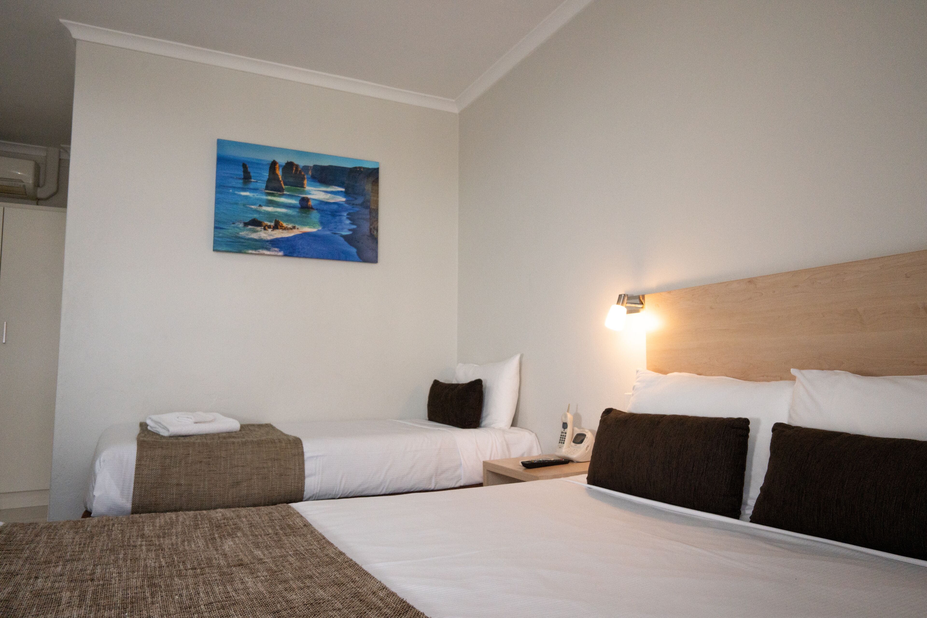 Een hotelkamer met twee eenpersoonsbedden, een schilderij van een kustlandschap, een nachtkastje met een telefoon en een nachtlampje.