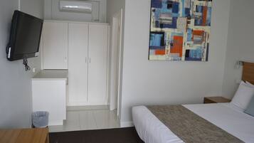 Une chambre d’hôtel avec un lit, un téléviseur fixé au mur, une armoire et un tableau.