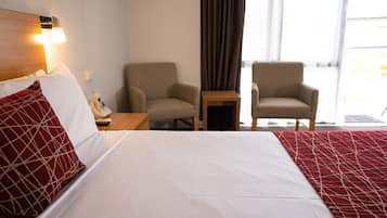 Ein Hotelzimmer mit einem großen Bett, zwei Sesseln, einem kleinen Tisch und einem Fenster mit Vorhängen.