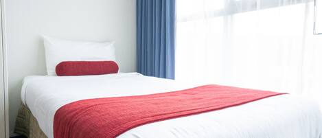 A neatly made bed with white and red bedding, a blue curtain, and a white wall.