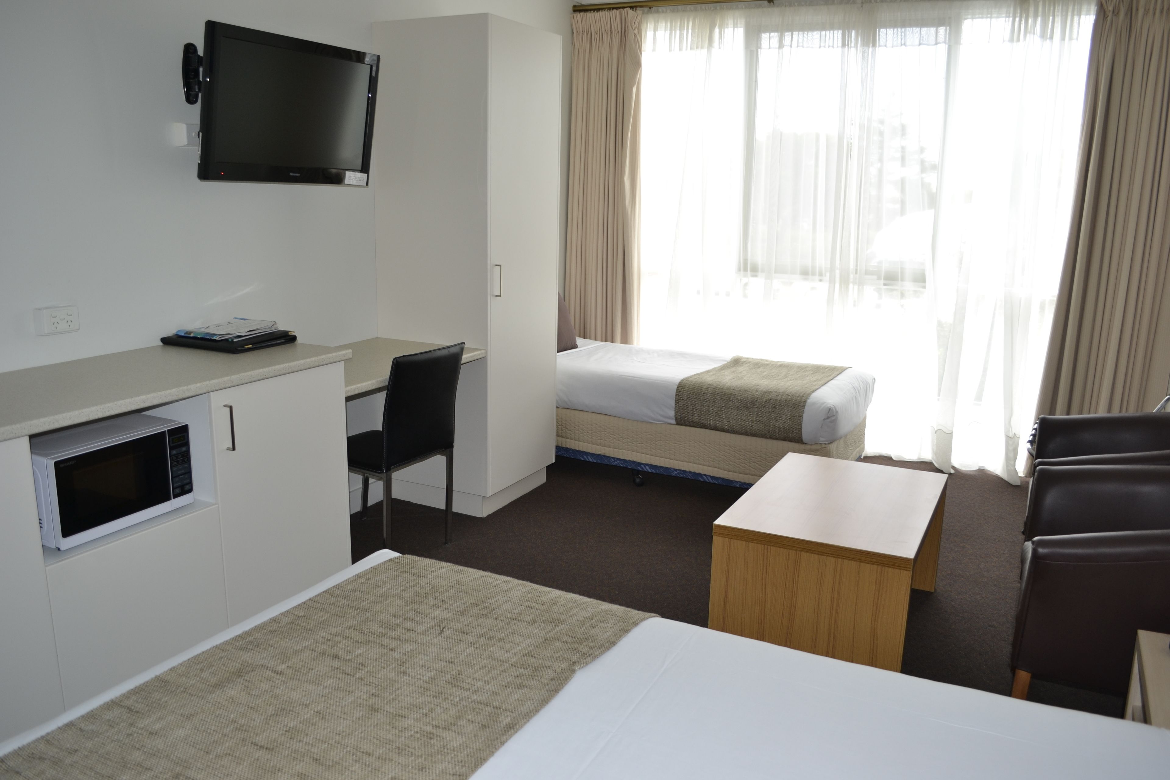 A hotel room with a bed, a desk, a chair, a TV, and a window with curtains.