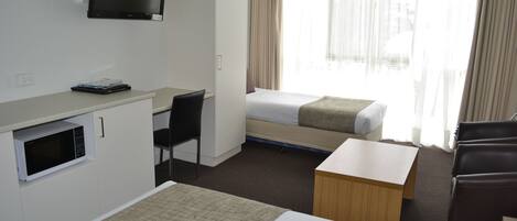A hotel room with a bed, a desk, a chair, a TV, and a window with curtains.