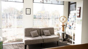 Una habitación con sofá, una mesita y un ventilador de pared. Se ve una ventana con vistas a una valla y árboles.