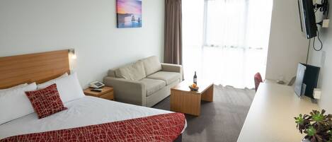 Habitación de hotel con cama, sofá, escritorio, mesa de centro y ventana con cortinas.
