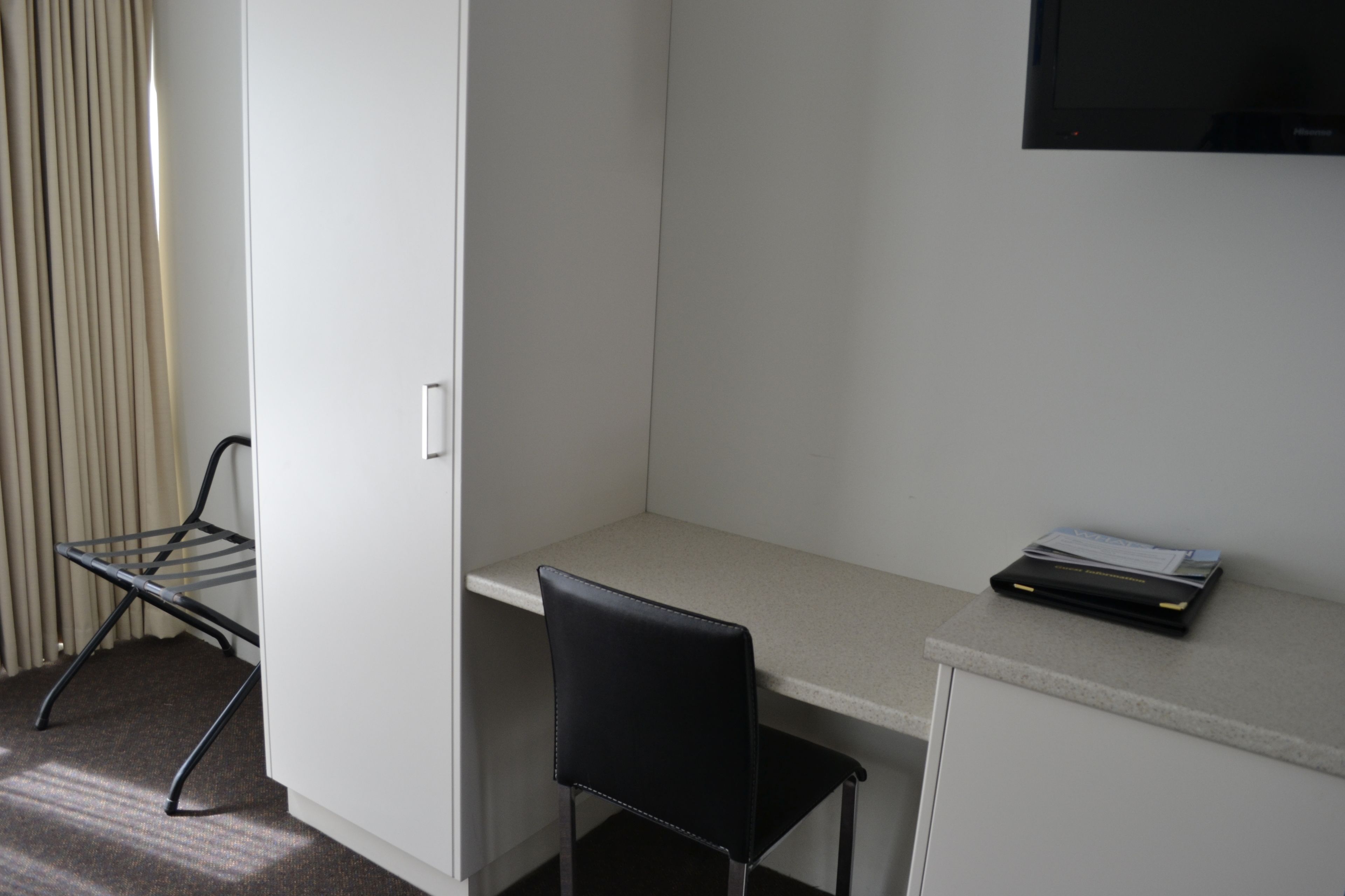 A small, private office with a desk, a chair, a radiator, and a television mounted on the wall.