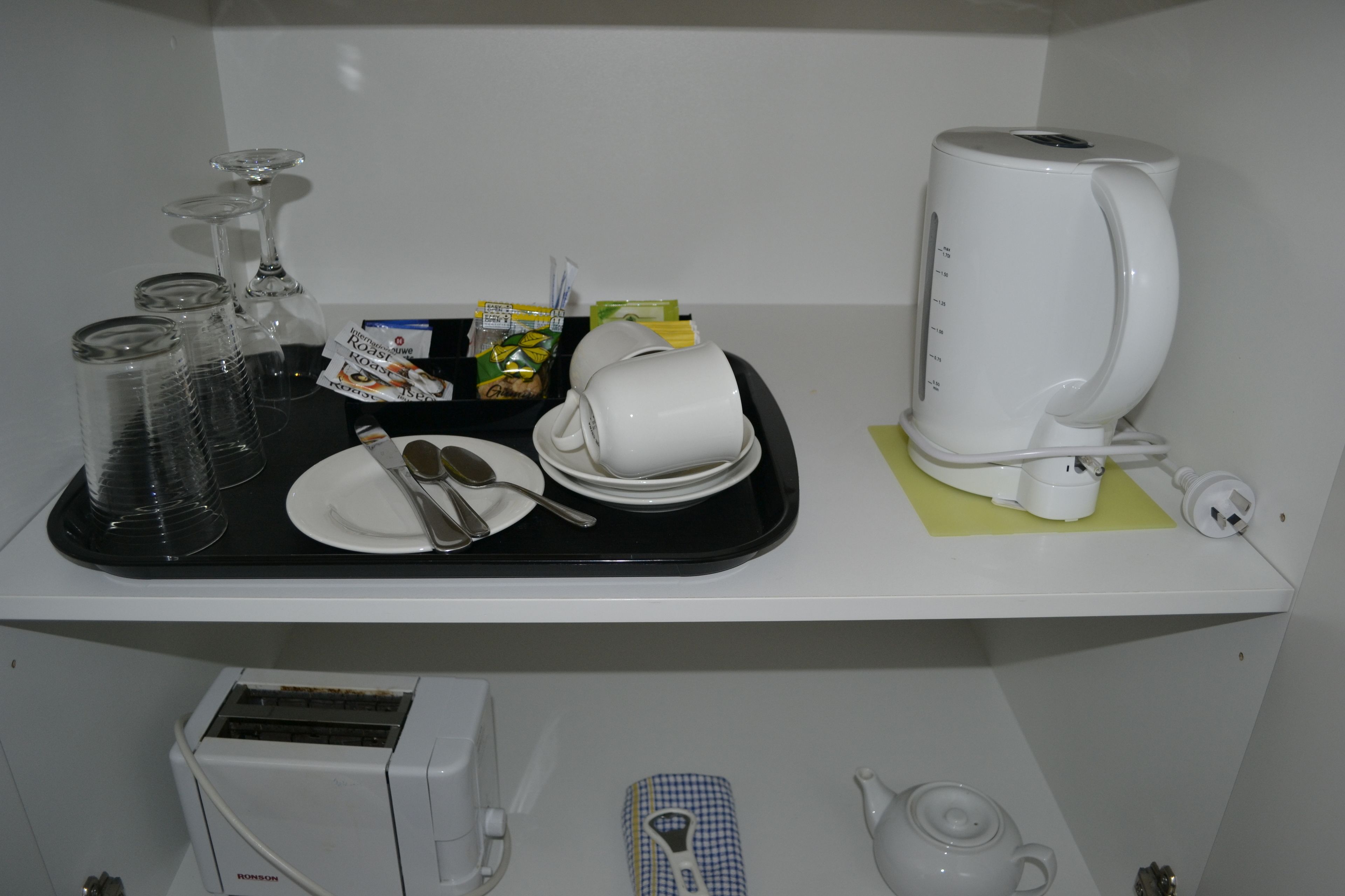 Un plateau contenant une cafetière, des tasses, des assiettes et des couverts, posé sur une étagère blanche.