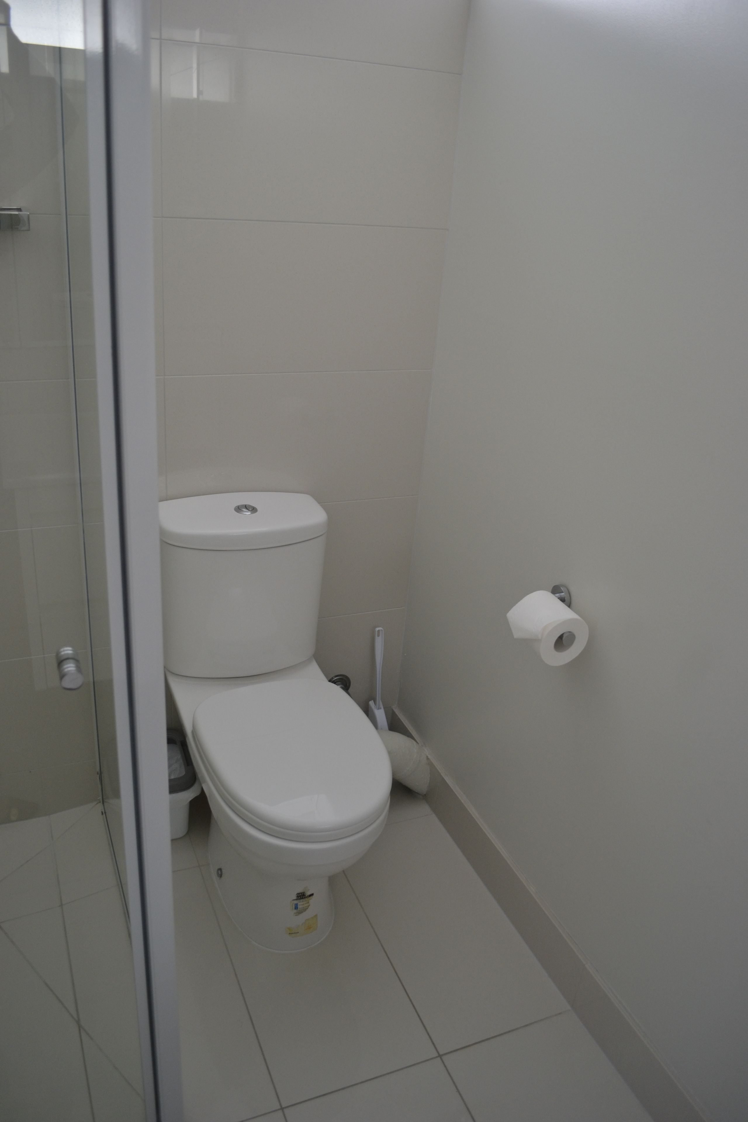 A bathroom with a toilet, a toilet paper holder, and a glass shower enclosure.