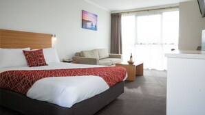 Habitación de hotel con una cama grande, un sofá, una mesita y una ventana con cortinas.